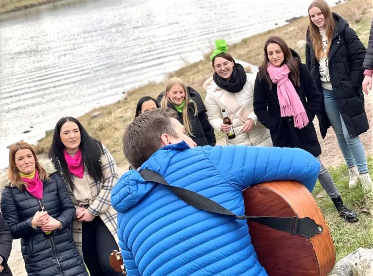 JGA-Koeln-Junggesellenabschied-Koeln-JGA-Singend Gitarrist mit Gitarre am Ufer vom Fluss Maas in Venlo mit Frauen auf einem Junggesellenabschied.