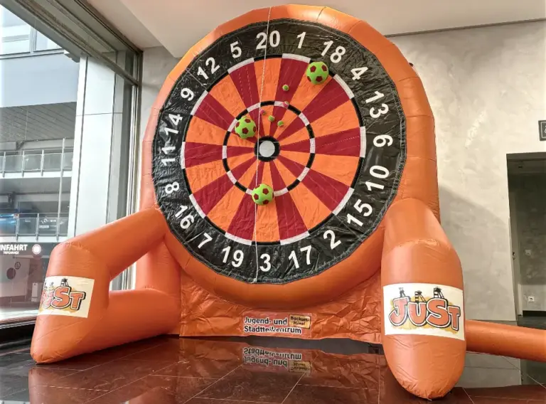 Aufblasbares Fußball-Darts-Modul – Individuelle Klett-Dartscheibe für Events Auf dem Bild ist ein hochwertiges, aufblasbares Fußball-Darts-Modul in Rundform zu sehen. Die überdimensionierte Dartscheibe besteht aus einer robusten Klettwand, auf der spezielle Fußbälle haften bleiben. Das Modul eignet sich ideal für Events, Firmenfeiern, Stadtfeste, Sportveranstaltungen und Kinderfeste. Das Fußball-Darts-Modul überzeugt durch seine stabile Konstruktion, die leuchtenden Farben und die große Trefferfläche, die für maximalen Spielspaß sorgt. Perfekt als Blickfang und sportliche Attraktion für Jung und Alt. Dieses individuell gebrandete Fußball-Darts-Modul zeigt beispielhaft, wie flexibel Gestaltung und Personalisierung möglich sind.