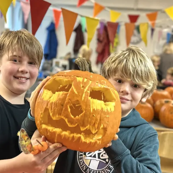 Ferienfreizeit-Herbst-Ferienbetreuung-Essen-Kürbisschnitzen Zwei Kinder auf Ferienfreizeit bei Deine Erlebnismacher aus Essen mit einem Kürbis in den Händen.