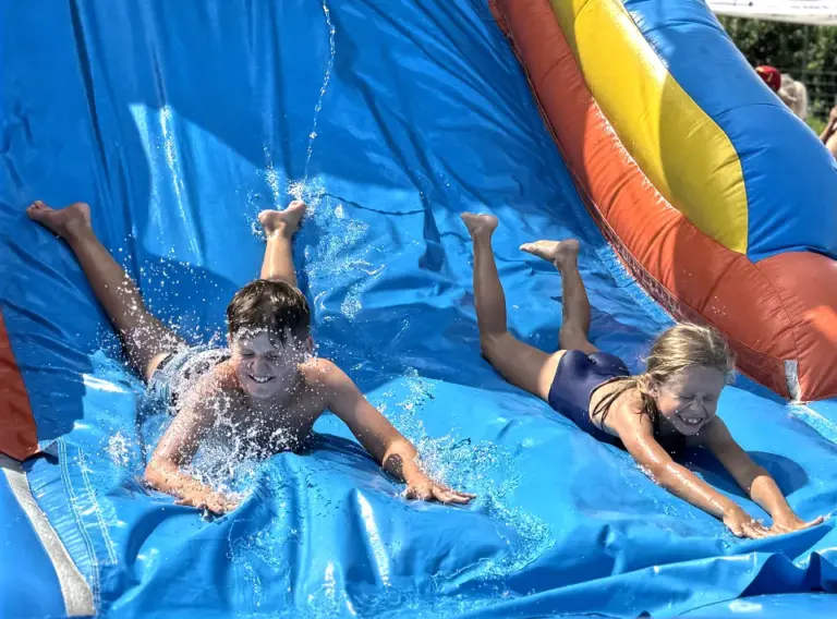 Ferienfreizeit Sommerferien-Ferienbetreuung Sommerferien-Feriencamp Essen Kinder auf einer XXL-Wasserhüpfburg mit Riesenrutsche während der Ferienfreizeit Essen auf den Sommerferien.