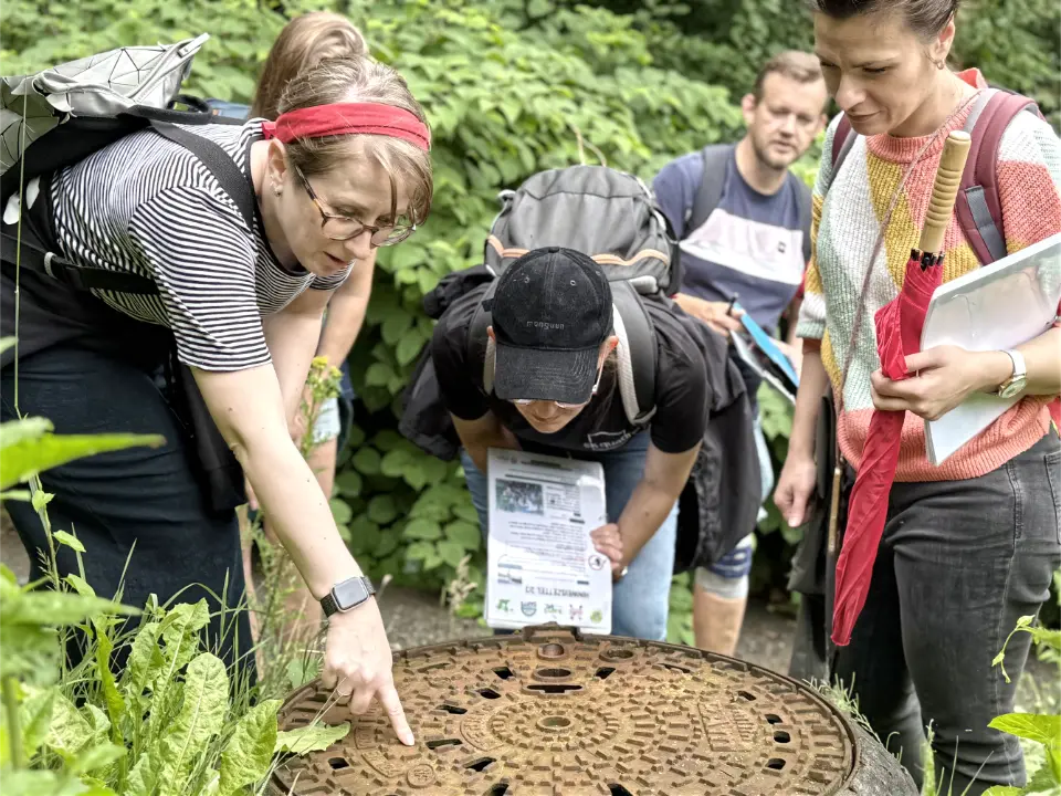 Männer und Frauen auf einer Schnitzeljagd in Essen beim Teambuilding-Event, die eine Lösung an einem Gullideckel gefunden haben.