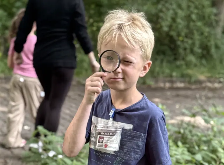 Schatzsuche-Kindergeburtstag-Detektivspiel-Spuernasen-Komissar Junge auf einem Kindergeburtstag bei einer Schatzsuche, wobei dieser mit einer Lupe in der Hand ausgestattet ist.