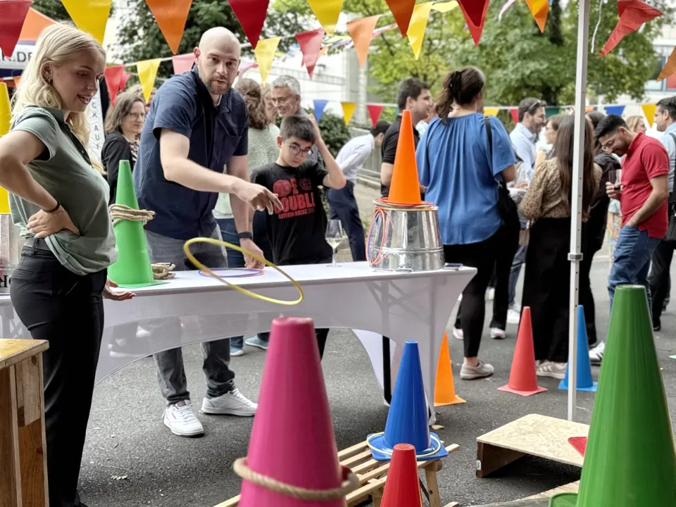 Menschen auf Firmenfeier beim Teambuilding-Event Jahrmarkt mit verschiedenen Jahrmarktständen, insbesondere Ringewerfen.