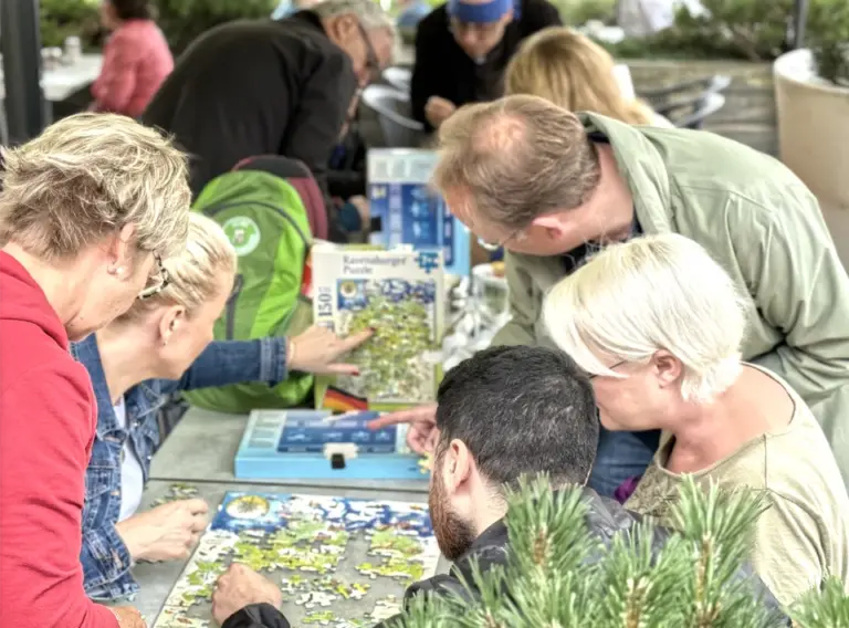 Teambuilding-Outdoor-Event-Schnitzeljagd-Firmenfeier Menschen auf Firmenfeier mit der Eventagentur "Deine Erlebnismacher" während des Teambuilding-Event Schnitzeljagd beim Puzzeln.
