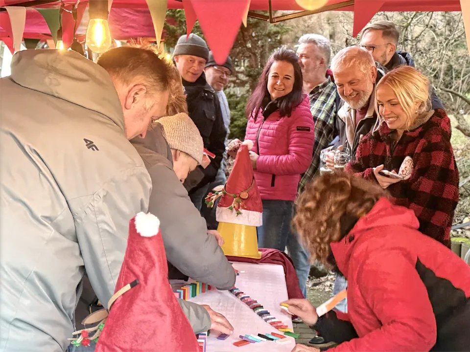 Weihnachtsfeier Oudoor auf welcher Teilnehmer eine kreative Teamaufgabe an einer weihnachtlich dekorierten Spielstation lösen während einer Winterolympiade.