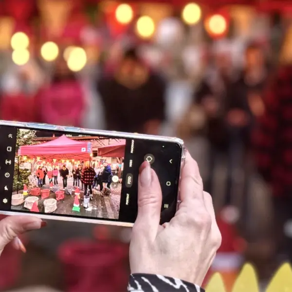 Smartphone zeigt eine Aufnahme vom Wintermarkt mit Gästen bei einer weihnachtlichen Firmenfeier.