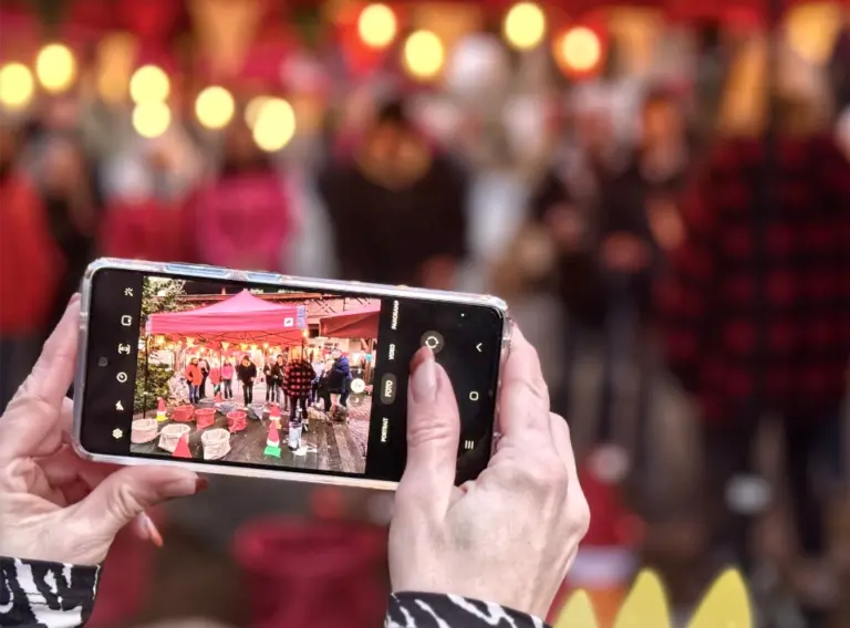 Momentaufnahme vom Wintermarkt bei einer weihnachtlichen Firmenfeier Smartphone zeigt eine Aufnahme vom Wintermarkt mit Gästen bei einer weihnachtlichen Firmenfeier.
