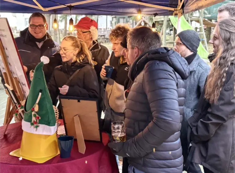 Weihnachtswerkstatt-Station bei Winterolympiade für Firmenfeiern Teilnehmende einer Winterolympiade betrachten eine Aufgabenstation in einer weihnachtlichen Outdoor-Werkstatt.