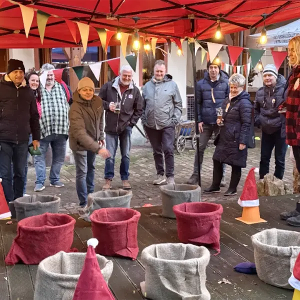 Teilnehmer einer Winterolympiade spielen ein Korbwurfspiel unter einem weihnachtlich dekorierten Pavillon.