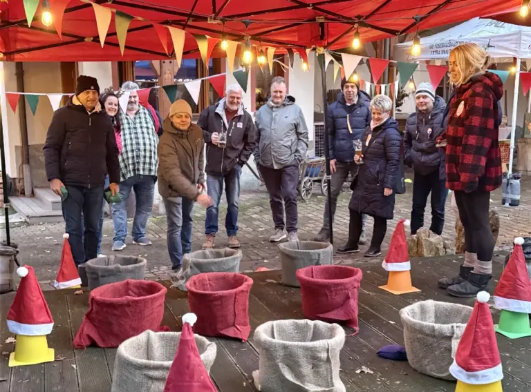 Winterliches Korbwurfspiel bei einer weihnachtlichen Winterolympiade Teilnehmer einer Winterolympiade spielen ein Korbwurfspiel unter einem weihnachtlich dekorierten Pavillon.