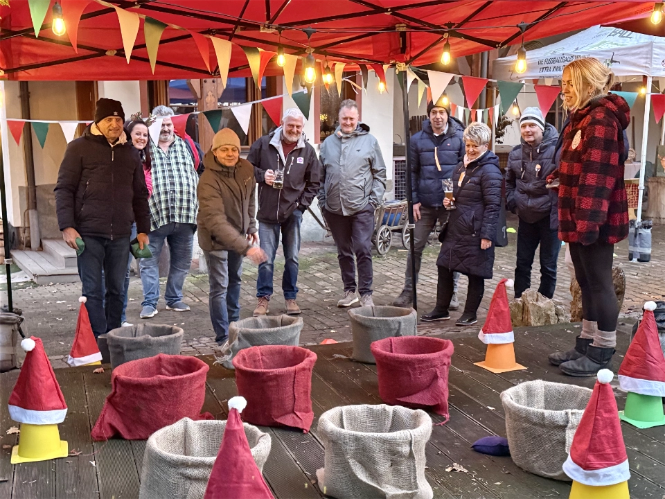 Teilnehmer einer Winterolympiade spielen ein Korbwurfspiel unter einem weihnachtlich dekorierten Pavillon.