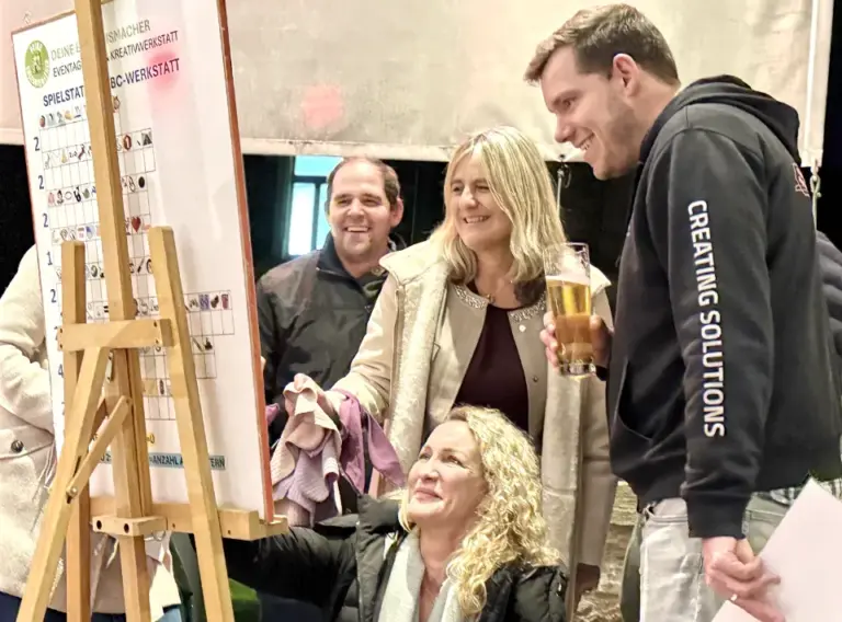 Winter Olympiade Weihnachtsfeier – Teambuilding-Spielstation in Karlsruhe Teilnehmende einer Winter Olympiade während einer deutschlandweit angebotenen Teambuilding-Weihnachtsfeier in Karlsruhe betrachten eine Spieltafel und freuen sich über die gemeinsamen Fortschritte.