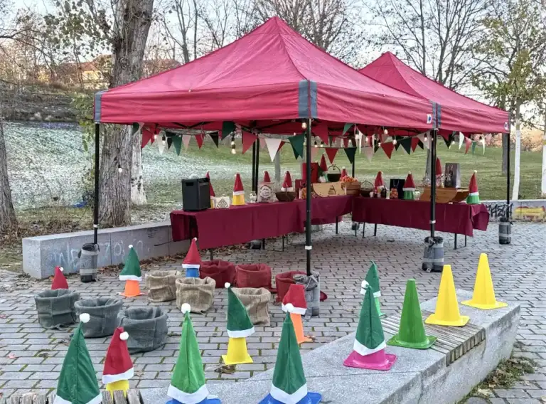 Glühweinwanderung-Firmenfeier-Winterevent Weihnachtlich dekorierte Spielstation bei einer Glühweinwanderung: Unter zwei roten Pavillons stehen Tische mit winterlicher Deko, umgeben von farbigen Hütchen, Säcken und kleinen Wichtelmützen für die Glühweinrallye.
