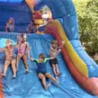 Fröhliche Kinder auf einer riesigen, aufgeblasenen Hüpfburg, die mit Wasser bespielt wird.
