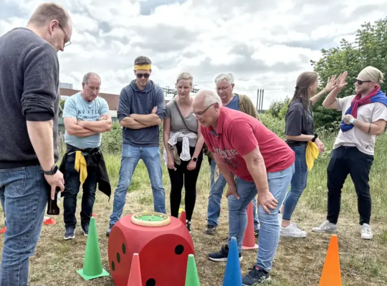 Sommerfest-Teambuilding-Firmenfeier-Teamspiele Menschen auf einem Betriebsausflug, die sich bei einem Spiel mit Würfeln konzentrieren und freuen.