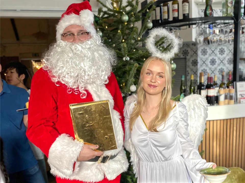 Weihnachtsmann und Weihnachtsengel stehen festlich gekleidet vor einem geschmückten Weihnachtsbaum bei einer Veranstaltung – Beispiel für Weihnachtsmann- und Engelbooking für Weihnachtsfeiern.