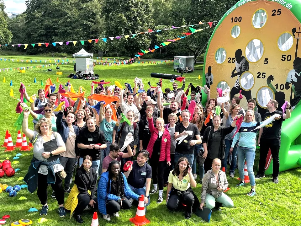 Teamolympiade für Firmen beim Sommerfest – große Gruppe von Mitarbeitern nimmt an Teamspielen im Park teil