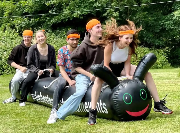 Aufblasbare Teamraupe beim Teambuilding – Gruppenspiel für Firmenevents Teilnehmer auf einer aufblasbaren Teamraupe beim Teambuilding für Firmenevents, Sommerfeste und aktive Gruppenspiele im Outdoor-Bereich.