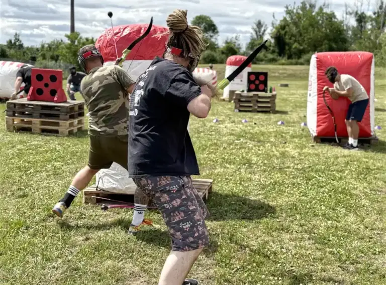 Arrow Games für Unternehmen – Actionreiches Outdoor-Event Mehrere Mitarbeitende spielen Arrow Games bei einem Outdoor-Event für Unternehmen und treten mit Pfeil und Bogen hinter aufblasbaren Hindernissen gegeneinander an