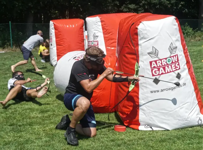 Arrow Tag Teambuilding für Unternehmen Mitarbeiter spielt Arrow Tag beim Teambuilding für Unternehmen und nutzt aufblasbare Hindernisse als Deckung auf dem Spielfeld