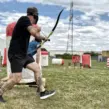 Mitarbeiter spielt mobiles Arrow Tag beim Outdoor-Firmenevent auf einem Spielfeld mit aufblasbaren Hindernissen und Pfeil und Bogen