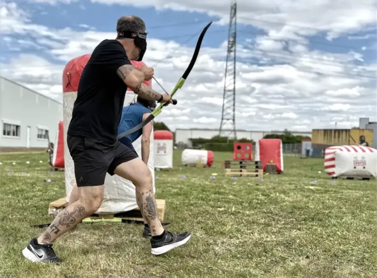 Mobiles Arrow Tag für Unternehmen beim Outdoor-Firmenevent Mitarbeiter spielt mobiles Arrow Tag beim Outdoor-Firmenevent auf einem Spielfeld mit aufblasbaren Hindernissen und Pfeil und Bogen