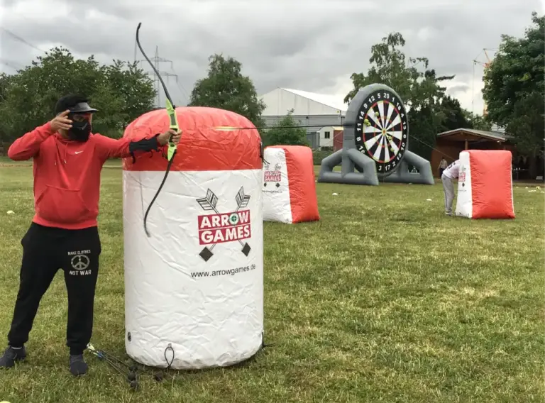 Mobiles Eventmodul mit Arrow Tag für Unternehmen Teilnehmer spielt mobiles Arrow Tag auf einem professionell aufgebauten Outdoor-Spielfeld mit aufblasbaren Hindernissen bei einem Firmenevent