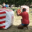 Teilnehmer spielt mobiles Arrow Tag bei einem Outdoor-Firmenevent in einer Parkanlage und nutzt aufblasbare Hindernisse als Deckung