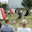 Mitarbeitende spielen Arrow Tag beim Sommerfest eines Unternehmens und weichen den gepolsterten Pfeilen auf einem Outdoor-Spielfeld aus