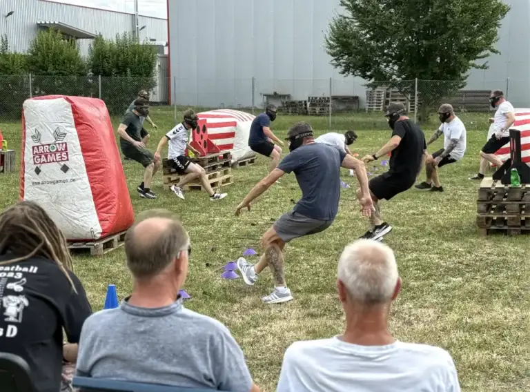 Arrow Tag beim Sommerfest für Unternehmen Mitarbeitende spielen Arrow Tag beim Sommerfest eines Unternehmens und weichen den gepolsterten Pfeilen auf einem Outdoor-Spielfeld aus