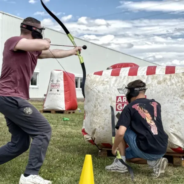 Zwei Mitarbeitende spielen mobiles Arrow Tag bei einem Team Event für Unternehmen und nutzen gemeinsam ein aufblasbares Hindernis als Deckung