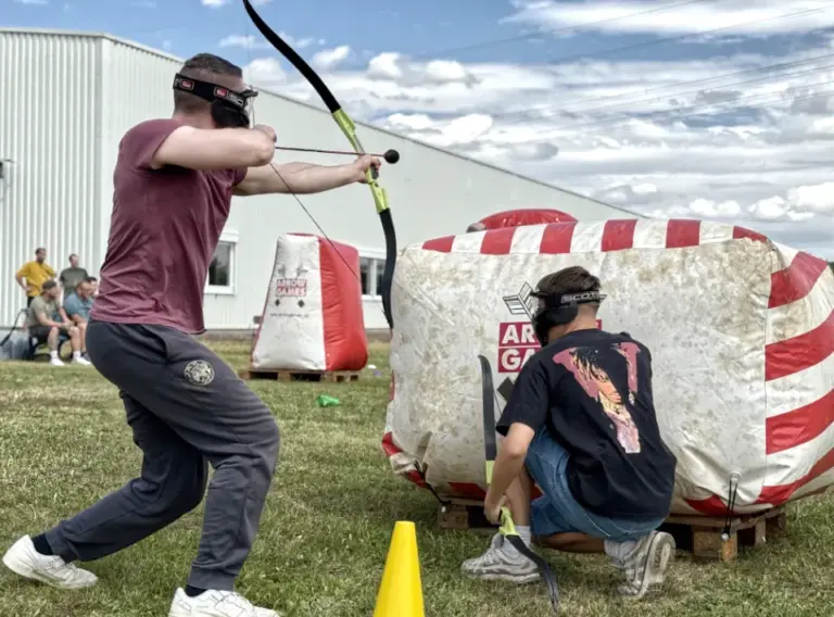 Zwei Mitarbeitende spielen mobiles Arrow Tag bei einem Team Event für Unternehmen und nutzen gemeinsam ein aufblasbares Hindernis als Deckung