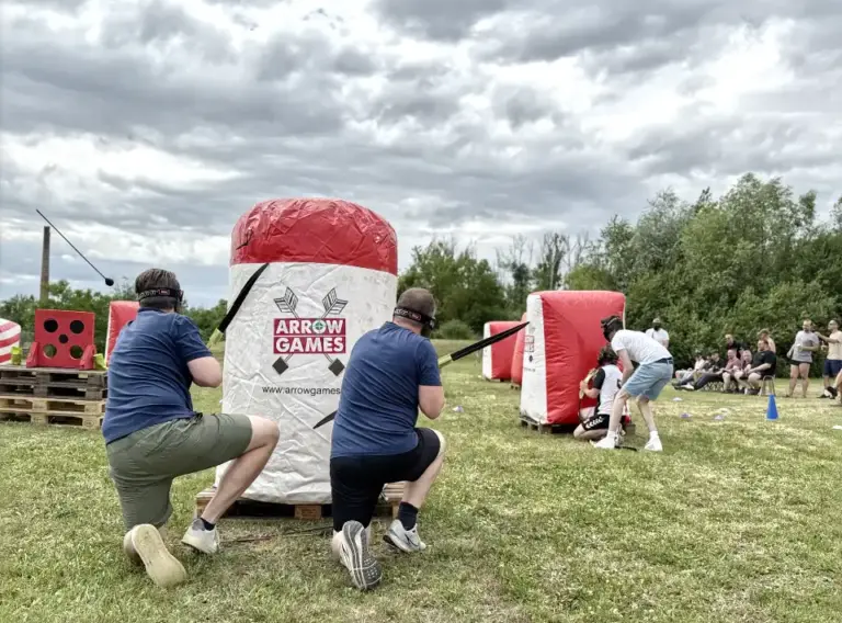 Teambuilding mit Arrow Tag beim Outdoor-Firmenevent Mitarbeitende spielen Arrow Tag beim Outdoor-Teambuilding für Unternehmen und nutzen aufblasbare Hindernisse für spannende Teamduelle